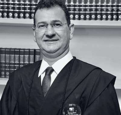 José Rawlinson Ferraz, sócio fundador do escritório, de beca diante de uma estante de livros jurídicos